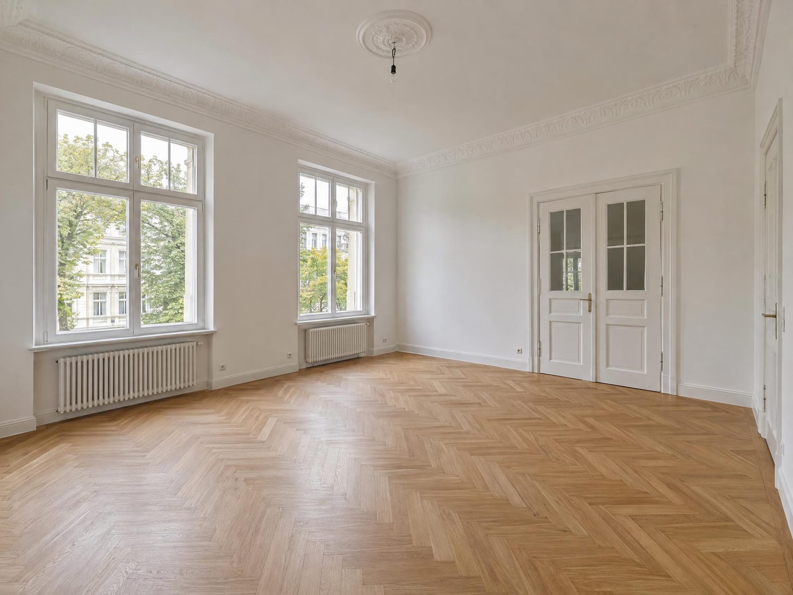 Vorher: leeres Altbau-Wohnzimmer mit Fischgrätparkett und zwei Sprossenfenstern, Blick schräg zur Flügeltür